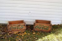 Two wooden Coca-Cola crates side by side, showing green logos and weathered wood.