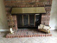 Full view of fireplace setup showing brass plated tool set on left, brass plated log holder with birch logs on right, brick fireplace and tile hearth.