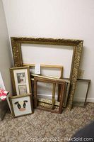 Photo showing multiple vintage frames leaning against a wall including large ornate gold frame and smaller frames in various styles and sizes