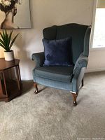 Blue wingback accent armchair displayed in a living room setting with decorative cushion and nearby furniture.