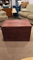 Front view of rectangular cherry stained wooden blanket box on carpeted floor.