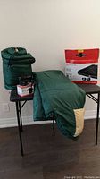 Full lot with two green sleeping bags, one rolled in a sack, queen air bed box, and small black electric pump on table.