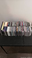 Over 80 assorted music CDs stacked on a black table, jewel cases and some box sets visible