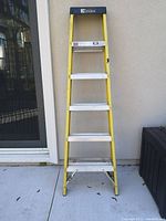 Front view of a 6 foot yellow Davidson step ladder with metal steps placed against a wall on a concrete floor.