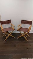 Two wooden folding director's chairs fully assembled and open, showing brown canvas seat and backrest and natural wood frame