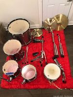 Overview of red drum shells, cymbals, stands and hardware laid on red blanket