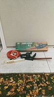 Full view of hedge trimmer, power bar, extension cord with hedge trimmer box in background