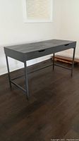 Full view of dark grey desk with two front drawers and metal legs on hardwood floor.
