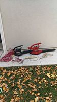 View of two electric leaf blowers, one black and one red, with extension cords and power bar on concrete surface.