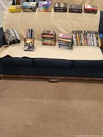 Wide view of over 60 DVDs arranged on a quilted beige blanket on a couch. Multiple stacks and rows showing the variety of DVDs and series included.