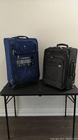 Two suitcases side by side on a black folding table against a white wall.