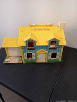 Closed exterior view of the yellow and blue vintage Fisher Price Play Family House with roof and windows visible.