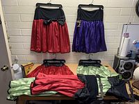 Photo showing seven satin skirts in red, purple, and green laid and hung up, highlighting their colors and waistband details.