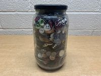 Front side of glass jar showing assorted vintage buttons through clear glass with black lid