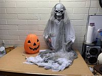 Front view of the Halloween skeleton and pumpkin decoration on a desk against a brick wall.