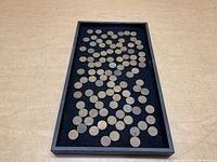 View of about 70 wheat pennies scattered in a black tray on a light wood surface.