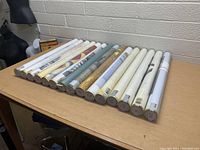 Photo of all 15 rolled art prints laid out on a table, showing ends of protective tubes with printed labels.