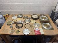 Wide shot of all vintage clock parts laid out on a wooden table showing various clock faces, bezels, glass covers, and clock hands.