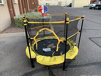 Front view of small kids trampoline with yellow padded edges, black mesh safety enclosure with zippered entry, and basketball hoop attachment.