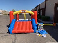 Photo showing front angled view of inflated Little Tikes bounce house with blower connected; accessories and box displayed outside