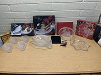 Overview of the lot showing a variety of Mikasa and Studio Nova glass dishes, including boxed items and multiple loose glass plates and bowls arranged on a table.