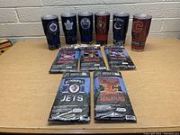 Seven NHL team tumblers and six sealed NHL vertical house flags arranged on table.