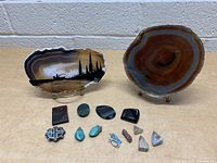 Lot of various decorative stones displayed on table including two large agate slices, one with a fishing scene painted in black on it, along with smaller polished stones and pendants.