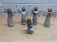 Five Willow Tree Angel figurines displayed on wooden surface, showing front view of each with wire wings and carved details