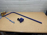 Photo of blue metal pet grooming arm with clamp and attached blue leash on a wooden surface against a white brick wall.