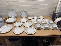 Set of Princess China dishes on a wooden table against a gray brick wall. The set includes plates of various sizes, teacups and saucers, and a serving platter, all decorated with a floral pattern and gold trim.
