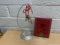 Photo of the Lenox Mickey Mouse Christmas ornament hanging from a silver metal stand beside its original red box with gold trim.