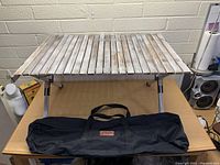 Folded camping picnic table with wooden top and metal legs, displayed on a table