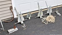Overview of five galvanized Danforth anchors with rope, chain, fish hook, boat hook and trailer tongue adapter on driveway