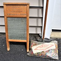 Front view of antique Columbus Ohio washboard alongside new Sla-Dust mop in package and mop handle.