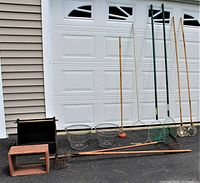 Full lot view showing clam rakes, scallop net, metal baskets, viewing boxes, and herring net basket arranged outside garage door.