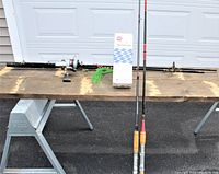 Overview image showing three fishing rods laid horizontally on a wooden plank: two boat rods and one spinning rod equipped with a reel. Also visible is the white box of the boat cover repair kit.