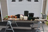 Overview of all items on a wooden plank supported by saw horses, including flower pots, watering can, pruning loppers, chair covers, and decorative pieces.