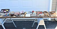 Overview of all sewing items arranged on a table outdoors including boxes of buttons, spools of thread, sewing needles and pins, embroidery hoops, crochet hooks and other tools.