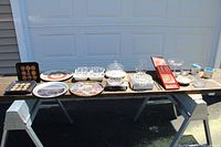 Wide view of entire lot on black table including trays, plates, bowls, glassware, and utensils