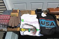 Photo showing ladies scarf, Isotoner gloves, women's sweatshirts with USA graphic and colorful text T-shirt, Dockers wallet, and evening purses.