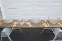 Seven scallop-shaped glass salad bowls, large Anchor Hocking punch bowl, ladle and fork displayed on a wooden surface.