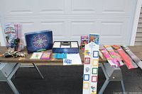 Full lot overview showing all items on a table including kites, games, books, growth measure, VHS tapes, and toys