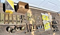 Full spread of vintage brass window sash locks and door hardware laid out on a table including boxed Ilco parts and loose brass knobs and latches.