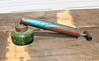 Bug sprayer with green glass base and blue patina metal nozzle on wooden surface