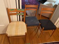 Three wooden chairs side by side, different upholstery colors.