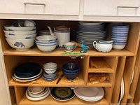 Wide view of assortment of blue and white bowls, plates, cups, creamer, and teapot on wooden shelves