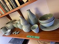 Shelf displaying various light green ceramic items including vases, bowls, plates, and butterfly decorations.
