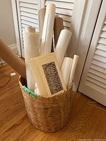 Woven rattan basket holding various rolled prints and posters, one visible John Snow lino-block print portfolio on top.