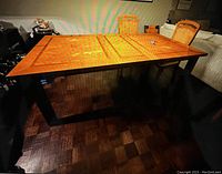 Wooden dining table with parquet pattern top and two leaves, one in use, surrounded by chairs.
