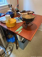Photo showing the rectangular wooden table with reddish-brown top and black legs, various kitchen items on top, and the leaf closed position.